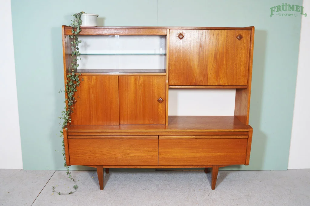 Een houten dressoir met verschillende kaste en plankdelen, een plant met klimgende ranken links, op de achtergrond een lichtgroene muur.