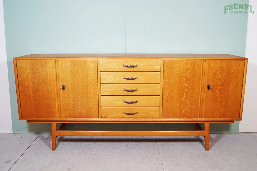 Een houten dressoir met vier laden en twee kasten, geplaatst tegen een groene muur.