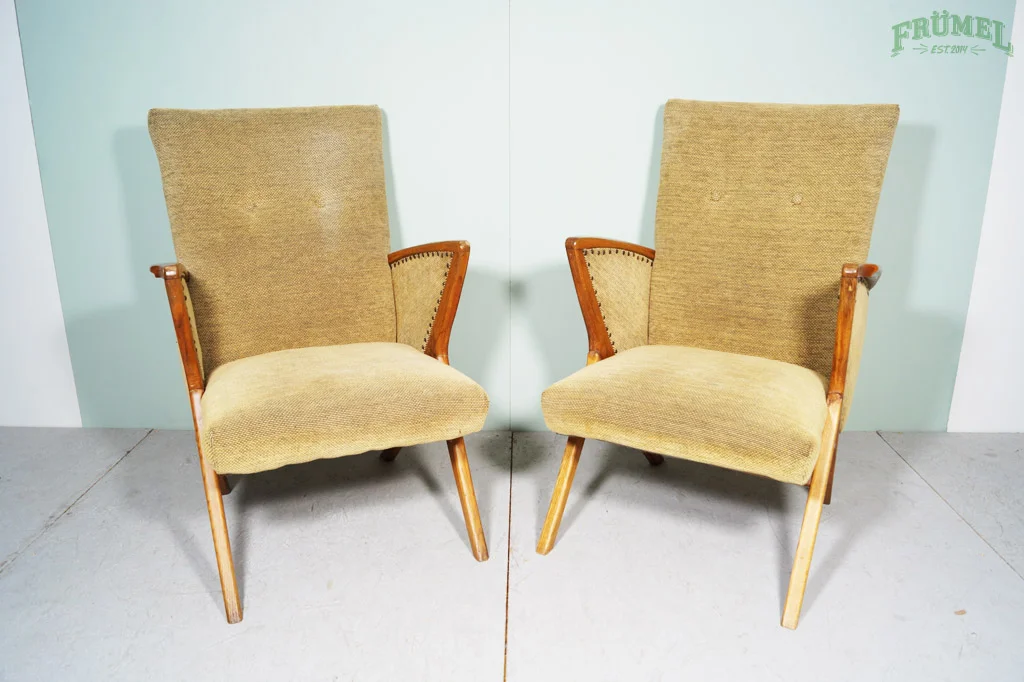Twee vintage gestoffeerde fauteuils met houten frame en armleuningen, geplaatst tegen een lichtgroene muur met het logo 'FRÜMEL' in de hoek.