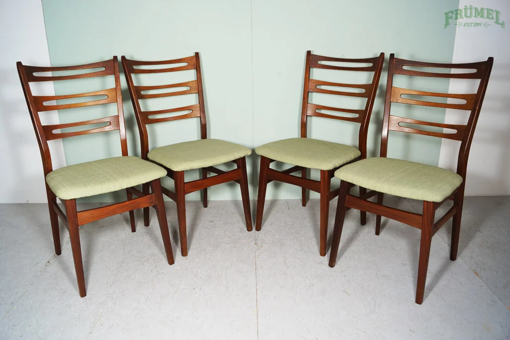 Vier houten eetkamerstoelen met groene zittingen, geplaatst in een hoek, met een witte en groene muur op de achtergrond.