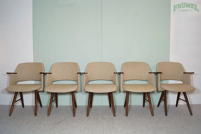 Zes beige stofgebonden stoelen met houten poten en armleuningen, netjes uitgelijnd tegen een lichte groene muur.