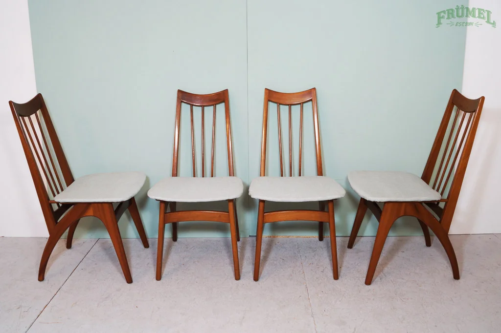 Vier houten eetkamerstoelen met beige zitkussens, op een lichte vloer, tegen een groene muur.