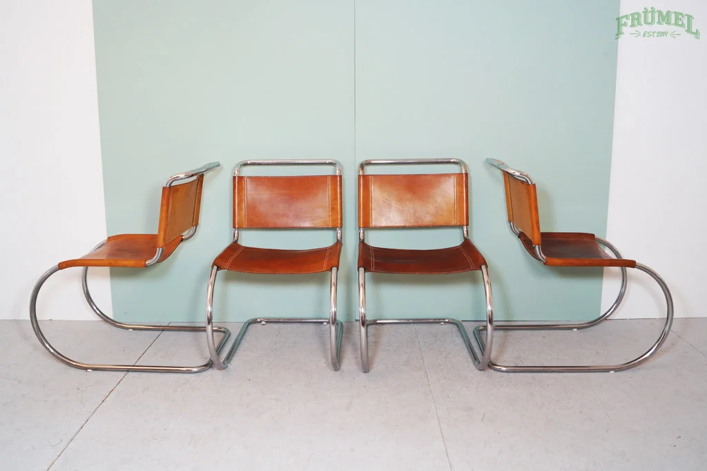 Vier vintage stoelen met leren zittingen en metalen frames, geplaatst tegen een mintgroene achtergrond in een wachtruimte.