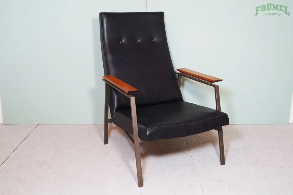 Een zwarte vintage leren stoel met houten armleuningen en metalen poten, geplaatst voor een lichtgroene muur.