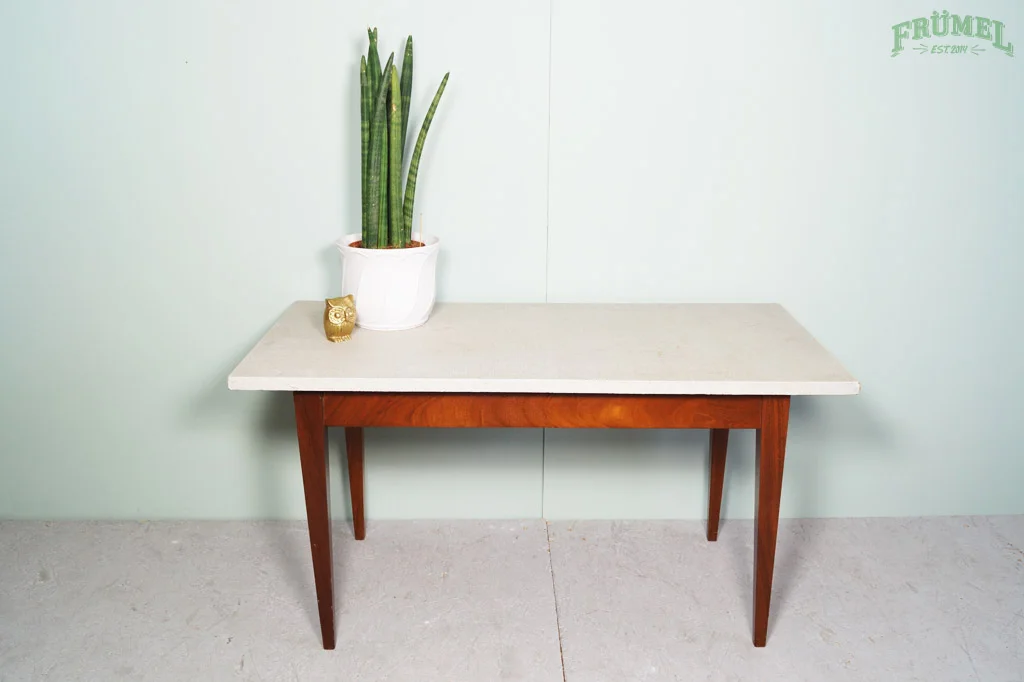 Een tafel met een witte pot met een groene plant en een gouden decoratief voorwerp op een lichtgroene muur.