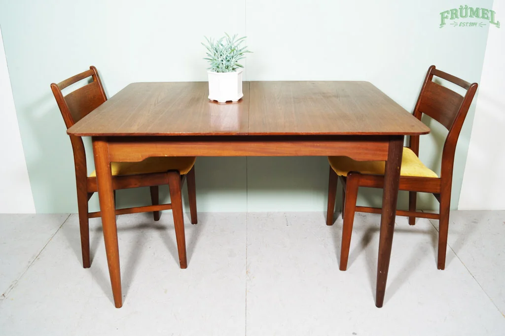 Houten eettafel met twee stoelen en een plantenpot met groen blad erop, in een lichte kamer.
