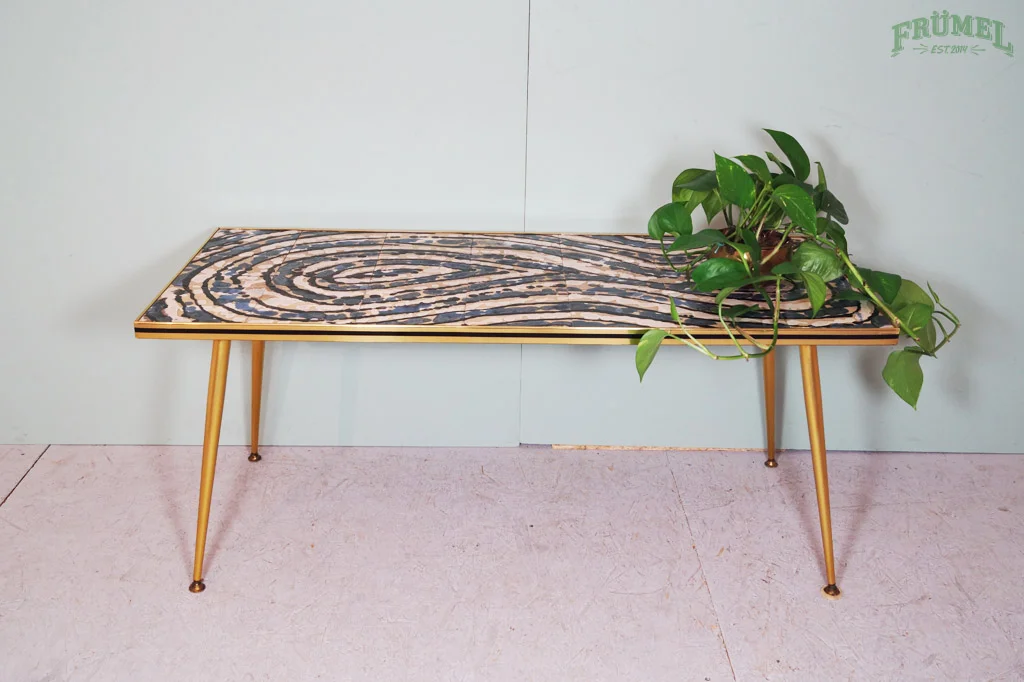 Een houten salontafel met een patroon op het blad, er ligt een hangende groene plant op de rechterkant