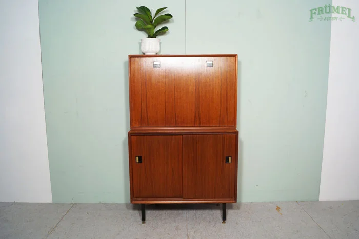 Houten kast met vier zwarte poten tegen een lichtgroene muur, met een groene plant in een witte pot bovenop.