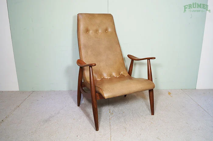 Lederen bijzetfauteuil met houten armleuningen en poten, geplaatst op een lichte tegelvloer voor een mintgroene muur.