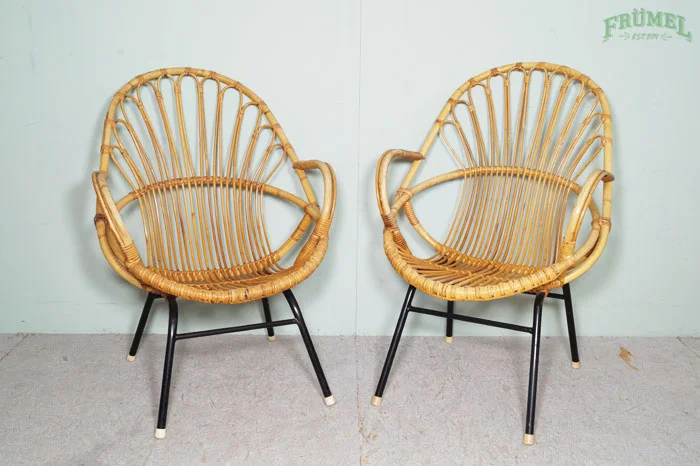 Twee rieten stoelen met zwart metalen poten staan tegen een witte muur