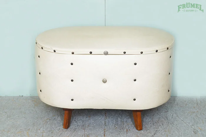 Wit vintage bank met houten poten voor schoenen, geplaatst tegen een lichtblauwe muur.