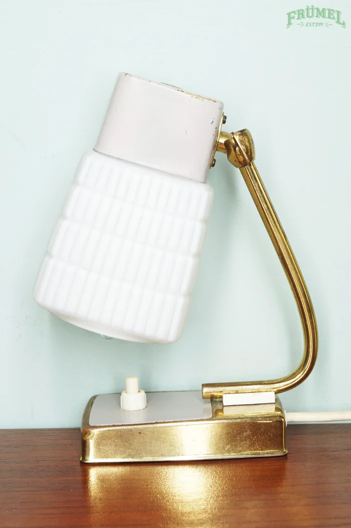 Vintage lamp met witte kap en gouden arm op houten tafel tegen lichte achtergrond.