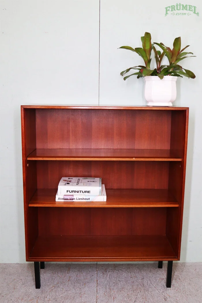 Een houten boekenkast met drie planken, met een groene plant in een witte pot op de kast en een paar boeken op de onderste plank.