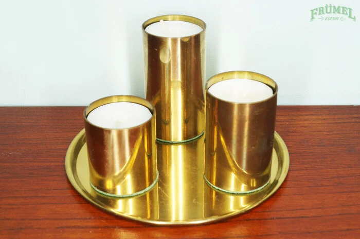 Drie vaakkaarsen in gouden houders op een goudkleurig dienblad op een houten tafel.