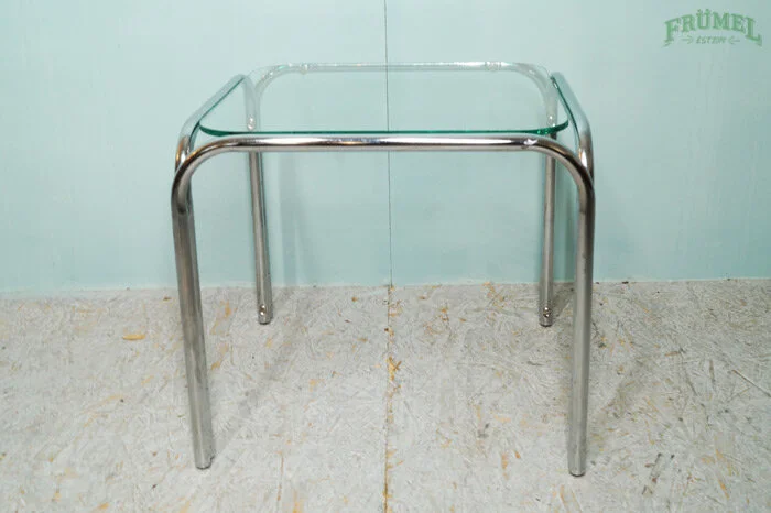Glazen tafel met metalen poten in een ruimte met lichtblauwe muren en een houten vloer.