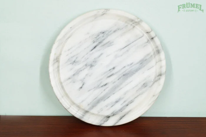 Leeg, rond marmeren serveerbord op een houten tafel en een lichte achtergrond met een groen logo in de rechterbovenhoek.
