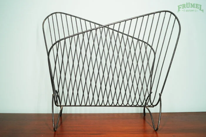 Metaalrek met schuine draden op een houten tafel, tegen een lichtgroene muur met groene tekst rechtsboven.