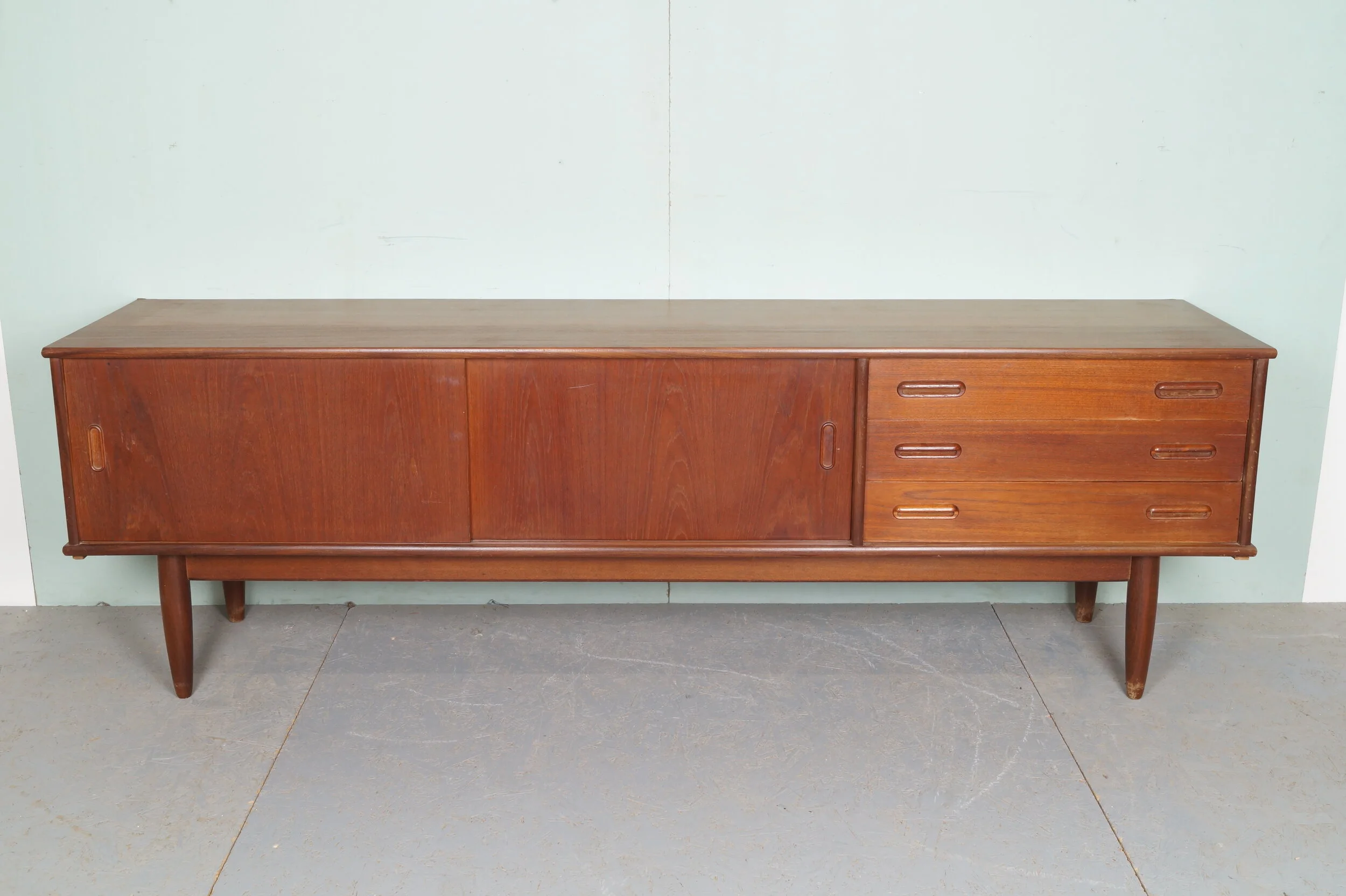 Houten vintage dressoir met schuifdeuren en drie lades op een betonnen vloer.