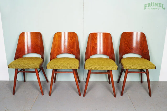 Vier houten stoelen met groene zitting stan in een rij tegen een lichtgroene muur.
