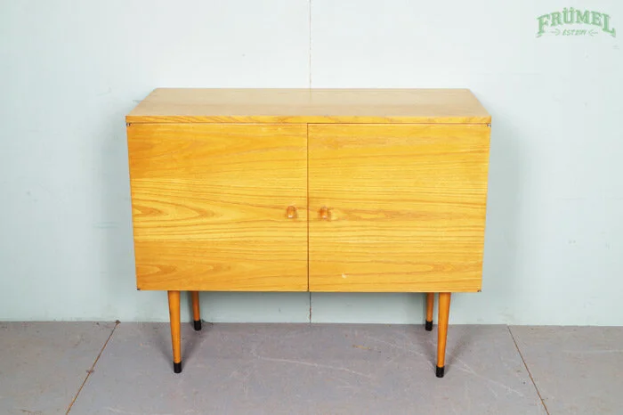 Houten kast met vier poten en twee deuren, geplaatst tegen een lichte muur.