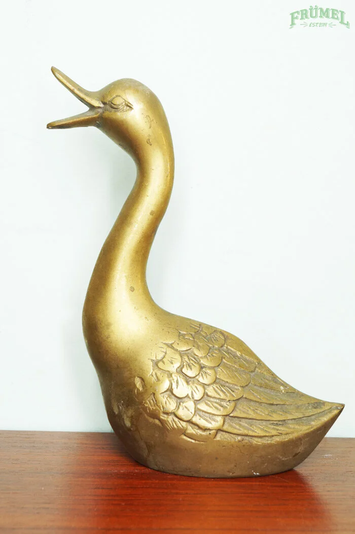 Gouden decoratieve beeld van een zwanen-achtig dier met een uitgespreide vleugel, geplaatst op een houten oppervlak.