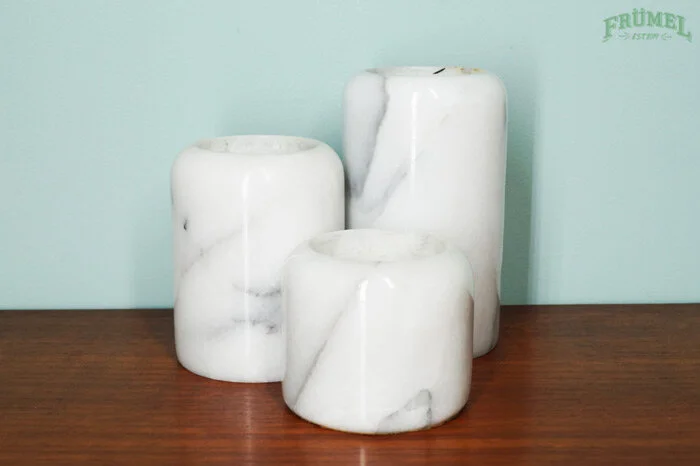 Drie witte marmeren vazen op een houten tafel, met een lichtgroene muur op de achtergrond.