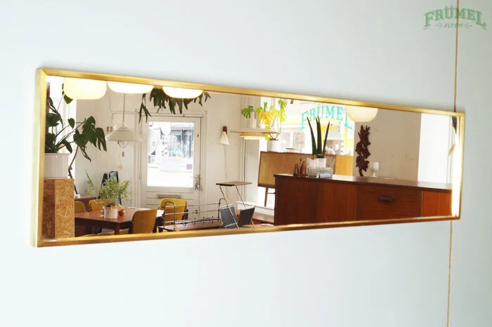 Binnenkant van een interieurwinkel of café, zichtbaar via een lang, horizontaal spiegel op een witte muur met 'FRÜMET' in groene letters.