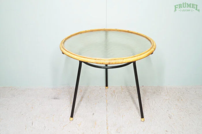 Ronde tafel met glazen blad en metalen poten tegen een lichtblauwe muur.