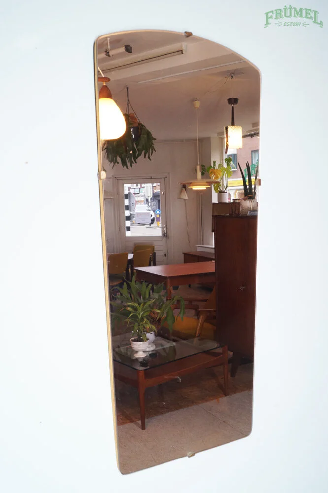 Binnenkant van een woon- of koffiehuis met houten meubels, planten, hanglampen en een spiegel die de kamer reflecteert.