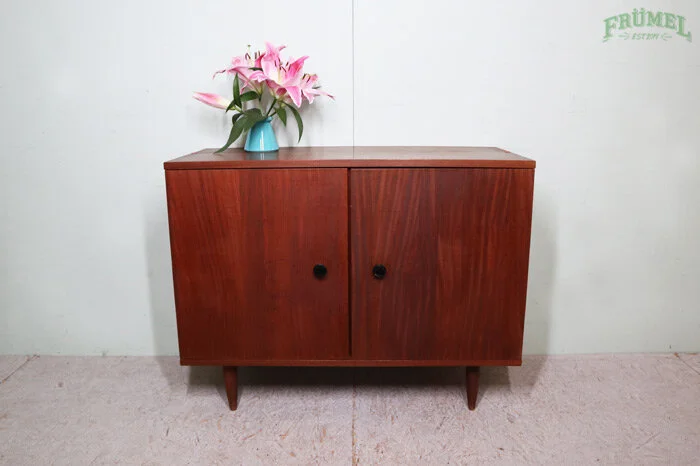 Houten kast met twee deuren, op de kast staat een blauwe vaas met roze en witte bloemen, tegen een witte muur