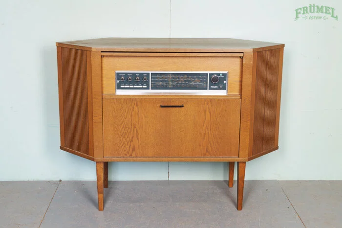 Vintage houten radio- en audio-televismeubel met schuifdeuren, staand op vier houten poten in een kamer met lichte muren.