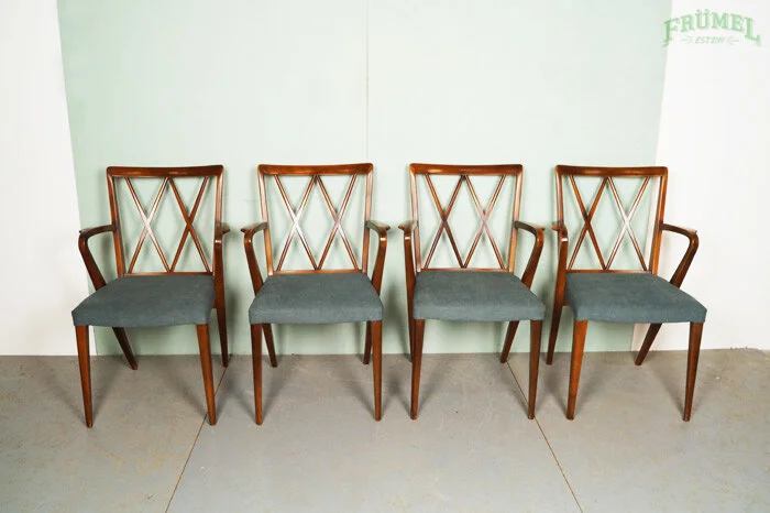 Vier houten stoelen met grijze zittingen tegen een lichte muur.