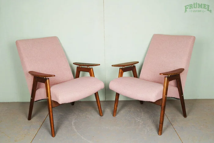 Twee vintage roze stoffeerde stoelen met houten armleuningen en poten, geplaatst tegen een lichtgroene muur.