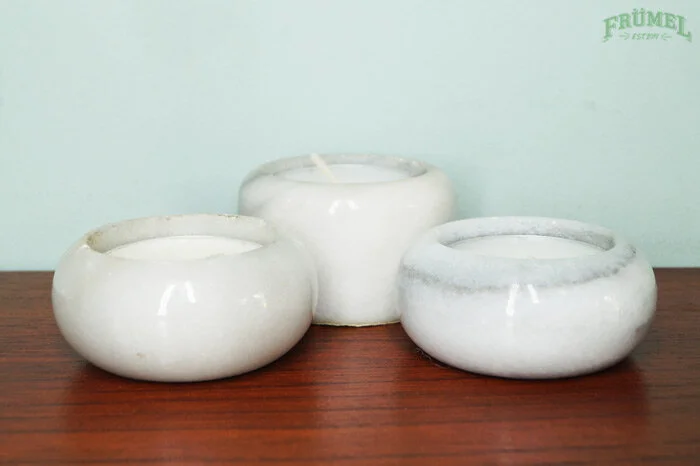 Drie witte kaarsen in keramische houders op een houten tafel