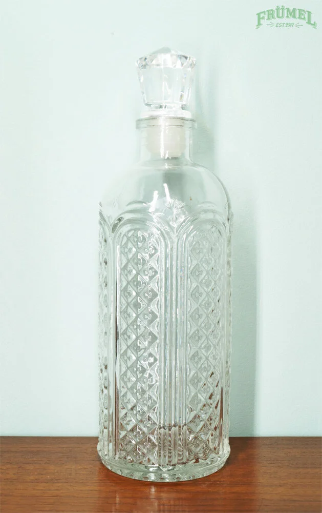 Een lege, decoratieve glazen fles met een facettenkristallen sluiting op een houten oppervlak.