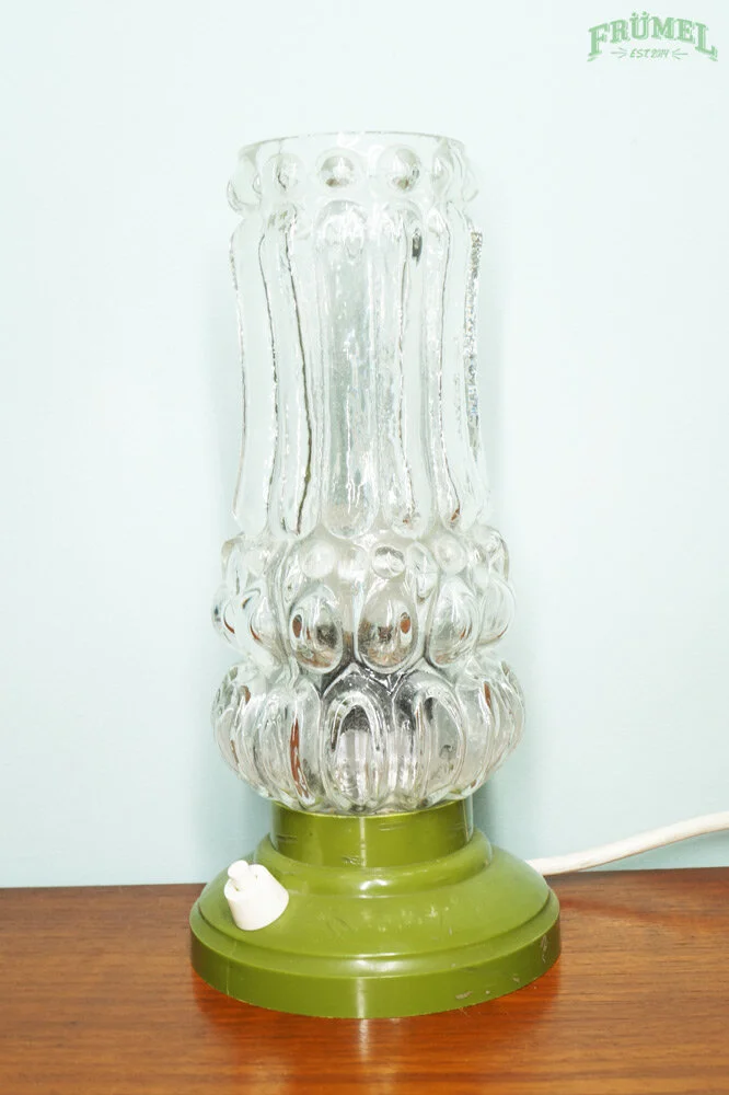 Een vintage wasd boterlamper met een groene onderkant en een glazen bovenkant op een houten tafel.