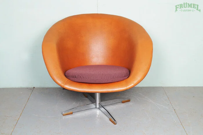 Oranje kuipstoel met een grijze kussen op een betonnen vloer voor een witte muur.
