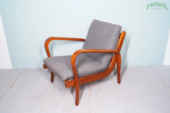 Houten fauteuil met grijze bekleding en polkadots, geplaatst tegen een witte muur.