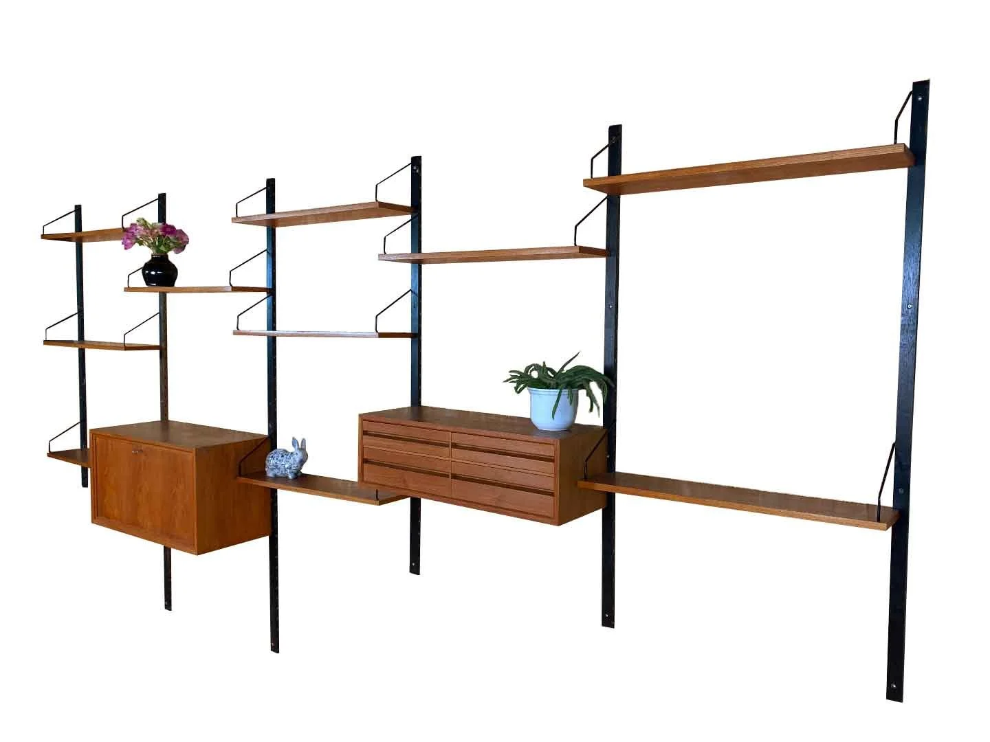 Teakhouten wandsysteem van Poul Cadovius met houten frame, metalen houders en houten planken, versierd met planten en decoratieve objecten.