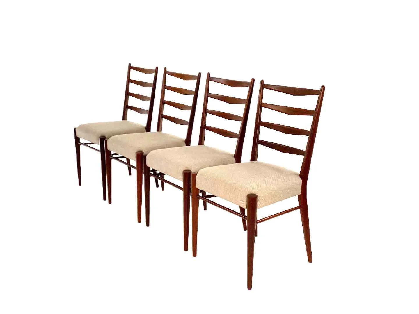 Vier houten Pastoe stoelen met beige zitkussens, uitgelijnd naast elkaar.
