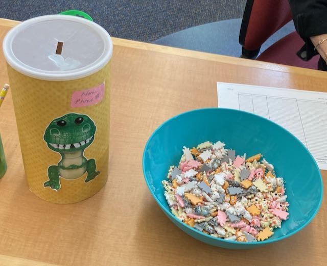 A raffle ticket canister for a chance to win REX sits beside a bowl of charms in the Children's Room