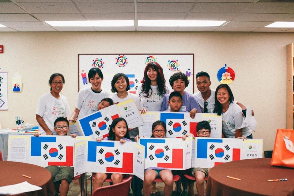 Children and adults adopted from Korea, along with Korean-American volunteers, are showing off Taegukki that they made with Sylvia Kim of the Washington Korean Paper Folding Institute