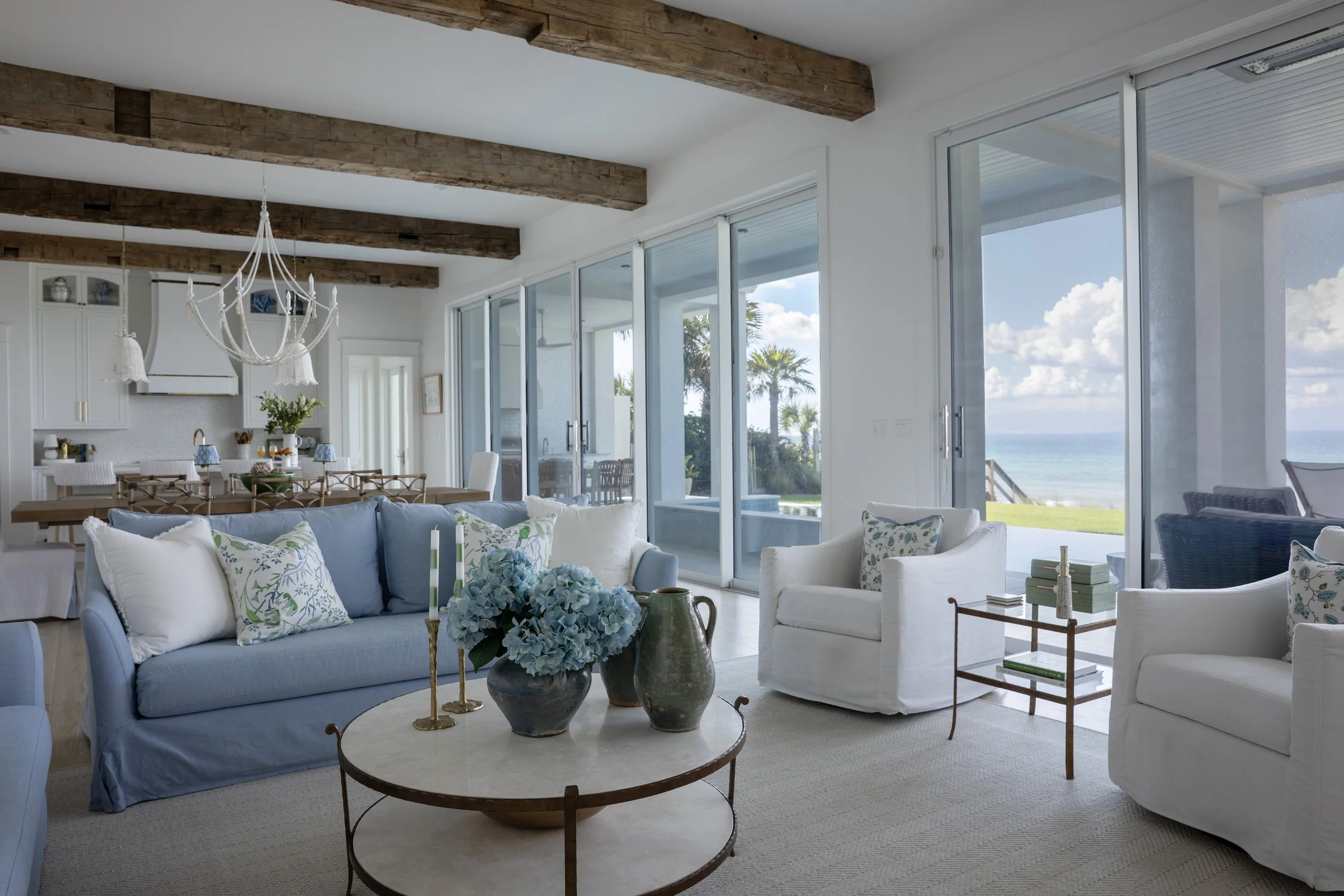 Open-concept coastal living and dining space in Blue Mountain Beach by Cindy McCarley Designs, featuring blue and white furnishings, reclaimed wood beams and panoramic Gulf views.