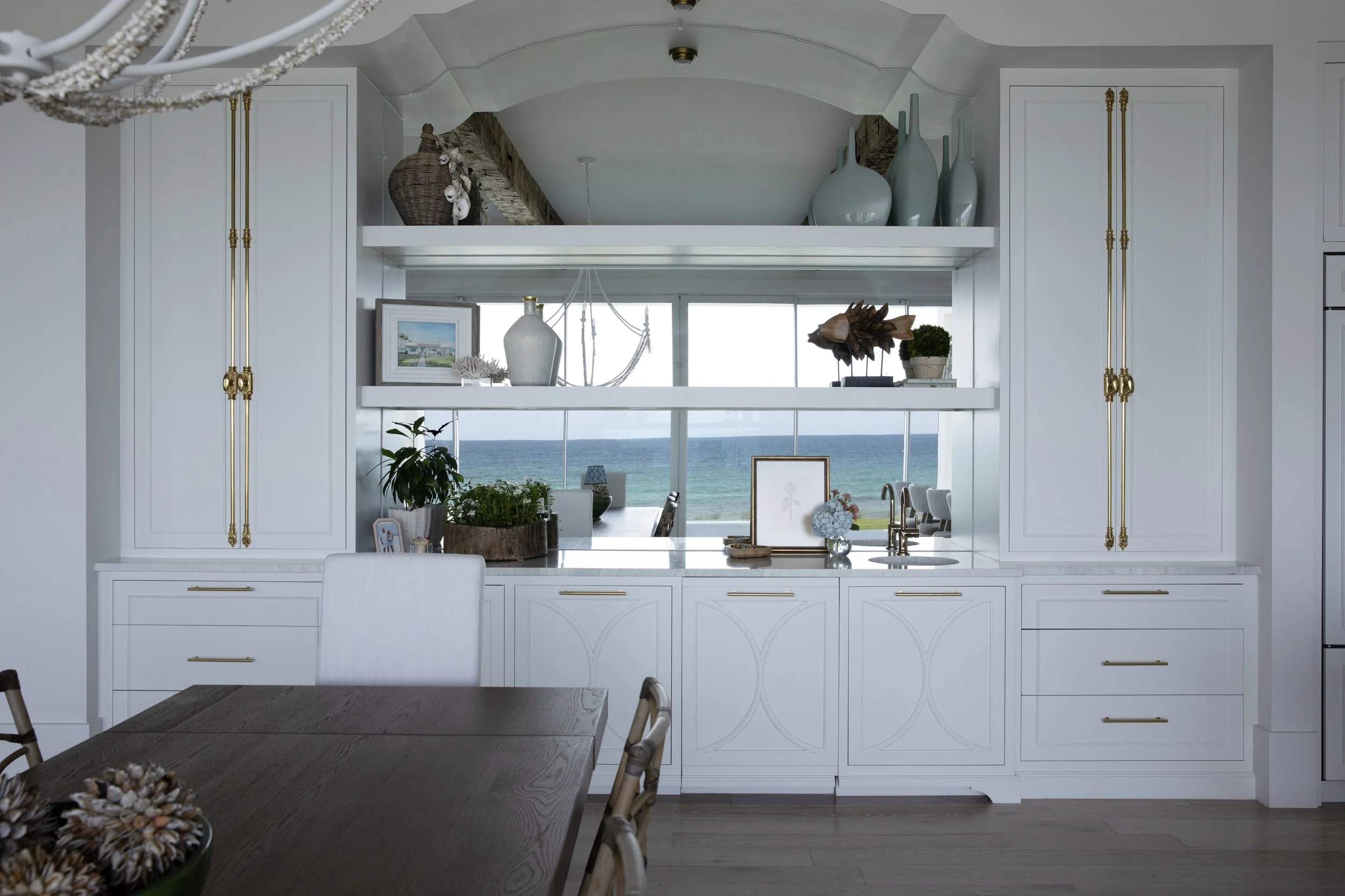 Custom dining room cabinetry in a Blue Mountain Beach home by Cindy McCarley Designs, featuring brass hardware, mirrored backsplash, styled open shelving and Gulf views.