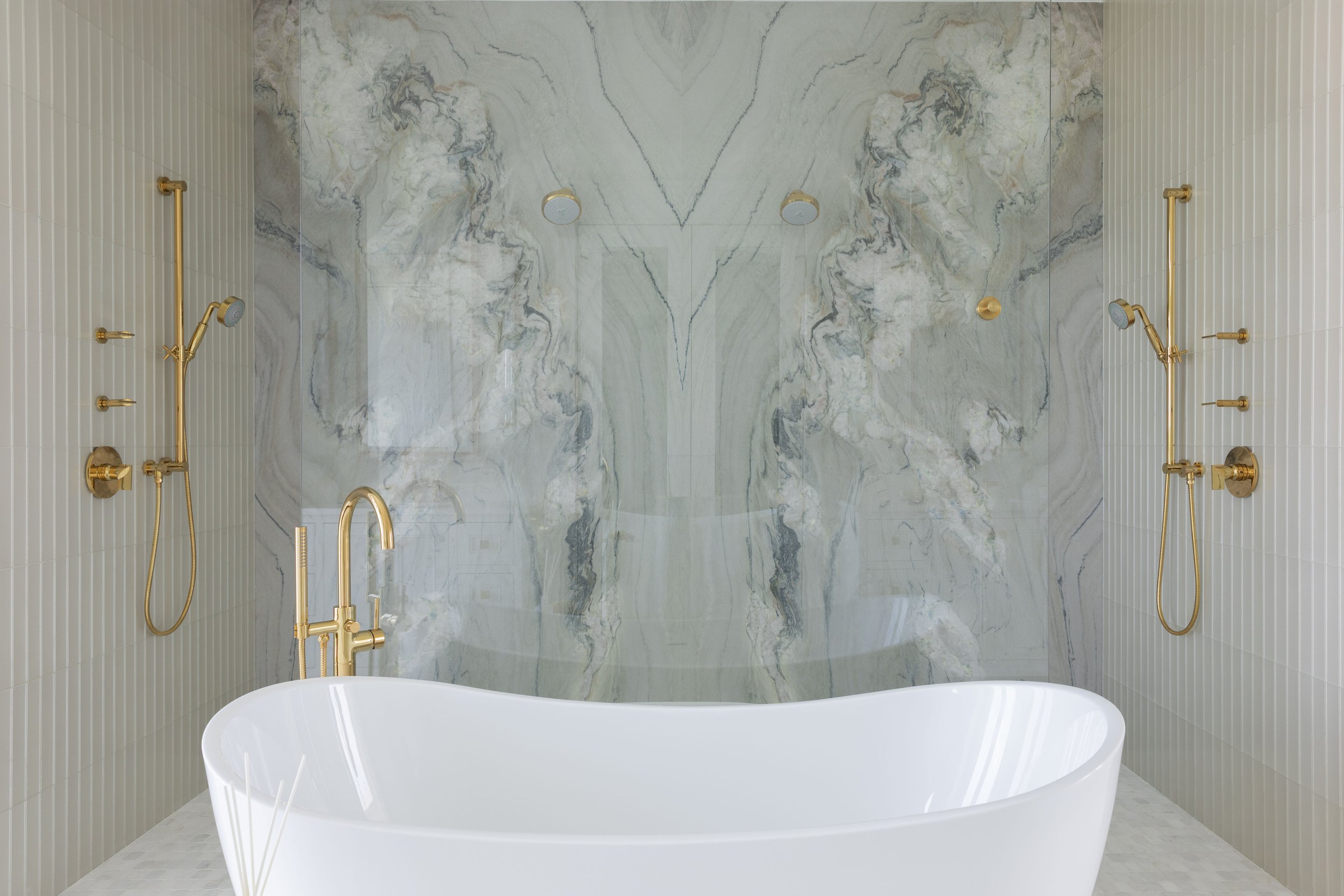 Luxury primary bathroom in Blue Mountain Beach by Cindy McCarley Designs, featuring a freestanding soaking tub, dramatic marble shower surround and brass fixtures.