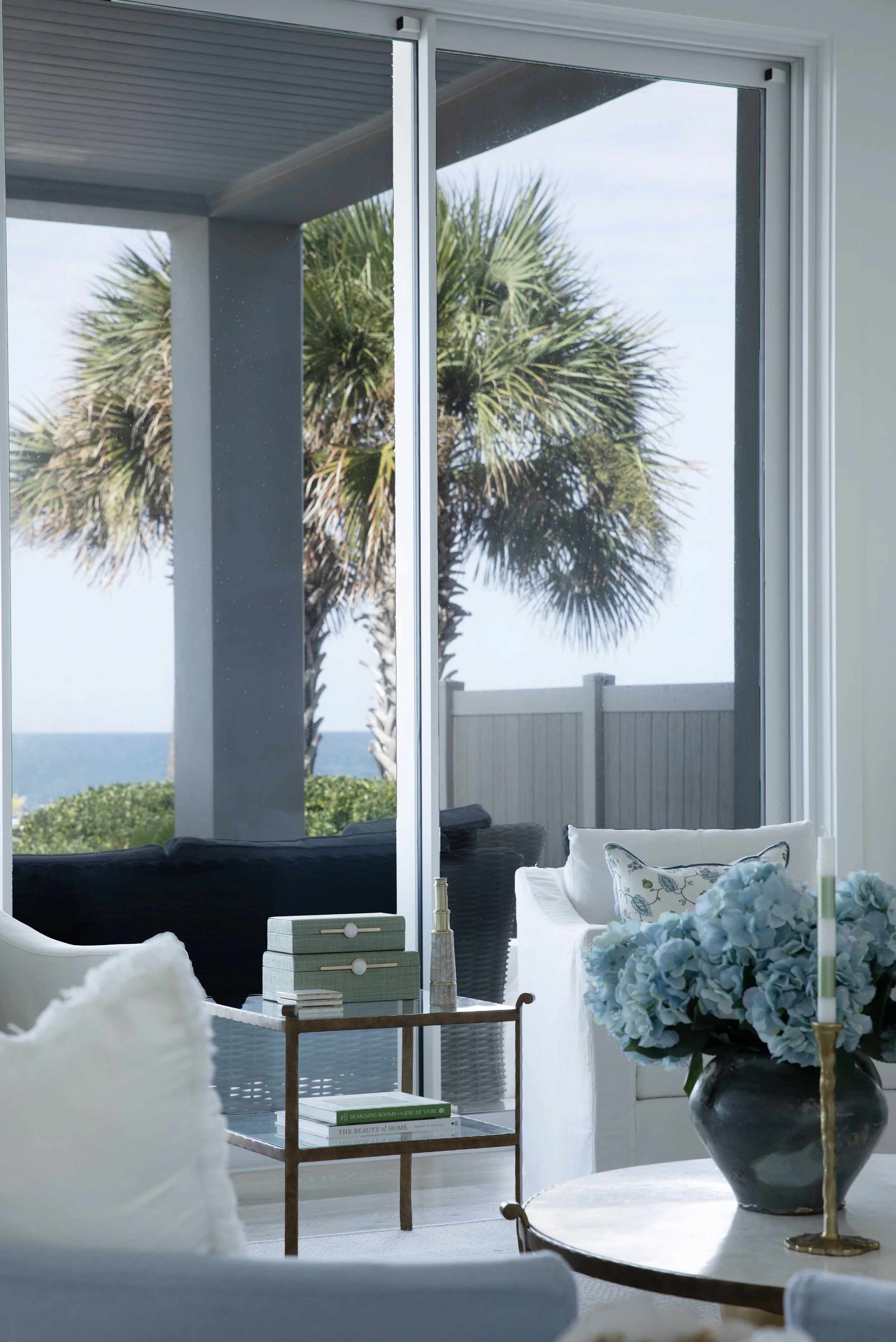 Blue Mountain Beach living room by Cindy McCarley Designs with blue hydrangeas, white seating and floor-to-ceiling windows overlooking palm trees and the Gulf.