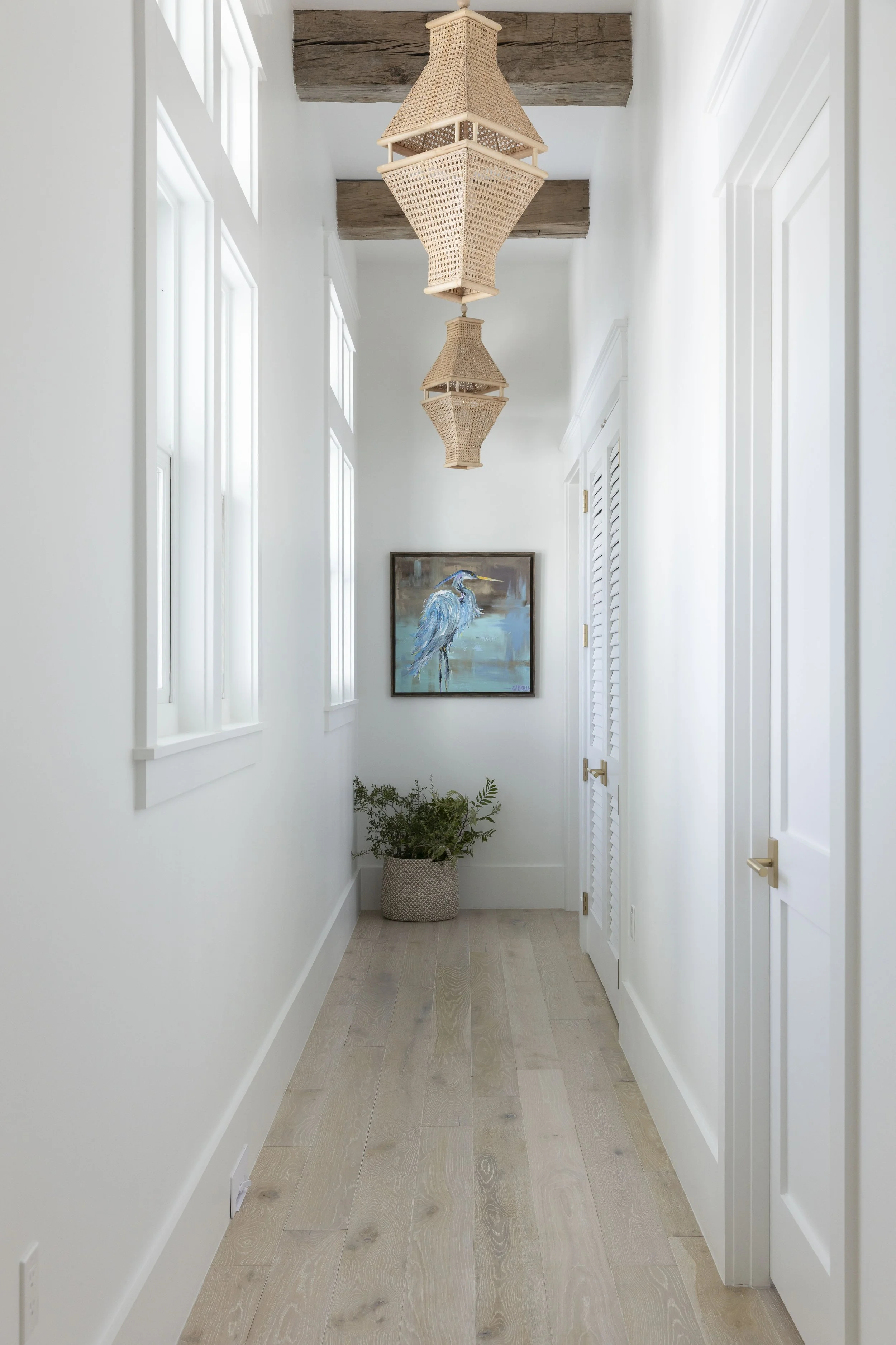 Light-filled hallway in a Blue Mountain Beach home by Cindy McCarley Designs, featuring woven pendant lights, reclaimed wood beams, coastal artwork and natural wood floors.
