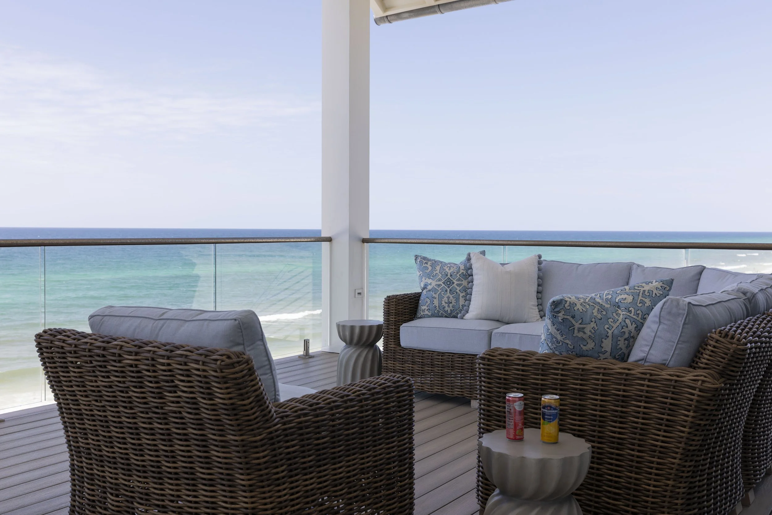Covered Gulf-front balcony in Blue Mountain Beach by Cindy McCarley Designs, featuring woven outdoor seating, blue coastal accents and panoramic ocean views.