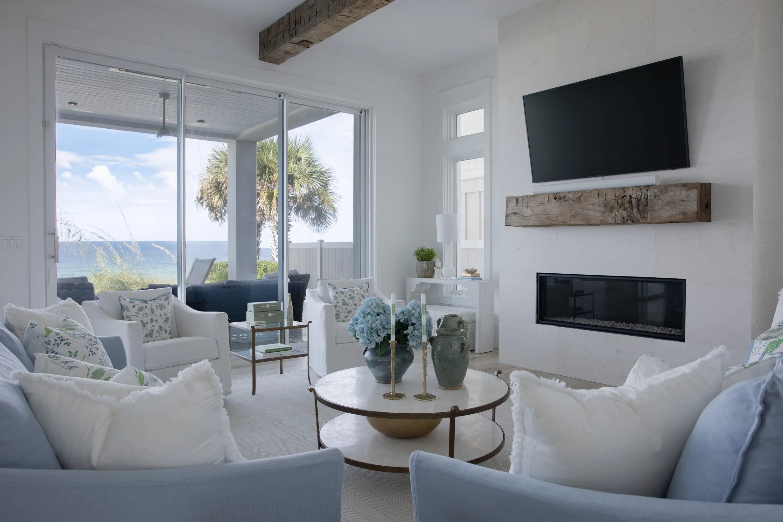 Coastal living room in Blue Mountain Beach by Cindy McCarley Designs, featuring soft blue and white furnishings, a limestone fireplace, reclaimed wood accents and Gulf views
