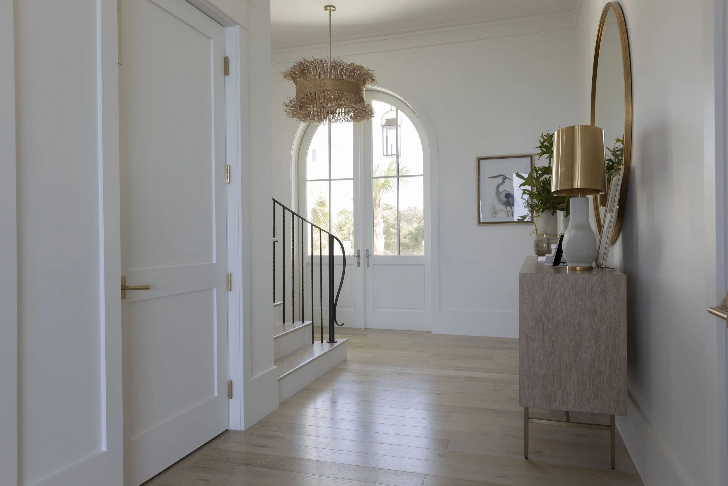 Coastal entryway in Blue Mountain Beach designed by Cindy McCarley Designs, featuring an arched glass door, woven pendant light, light wood floors and warm brass accents.